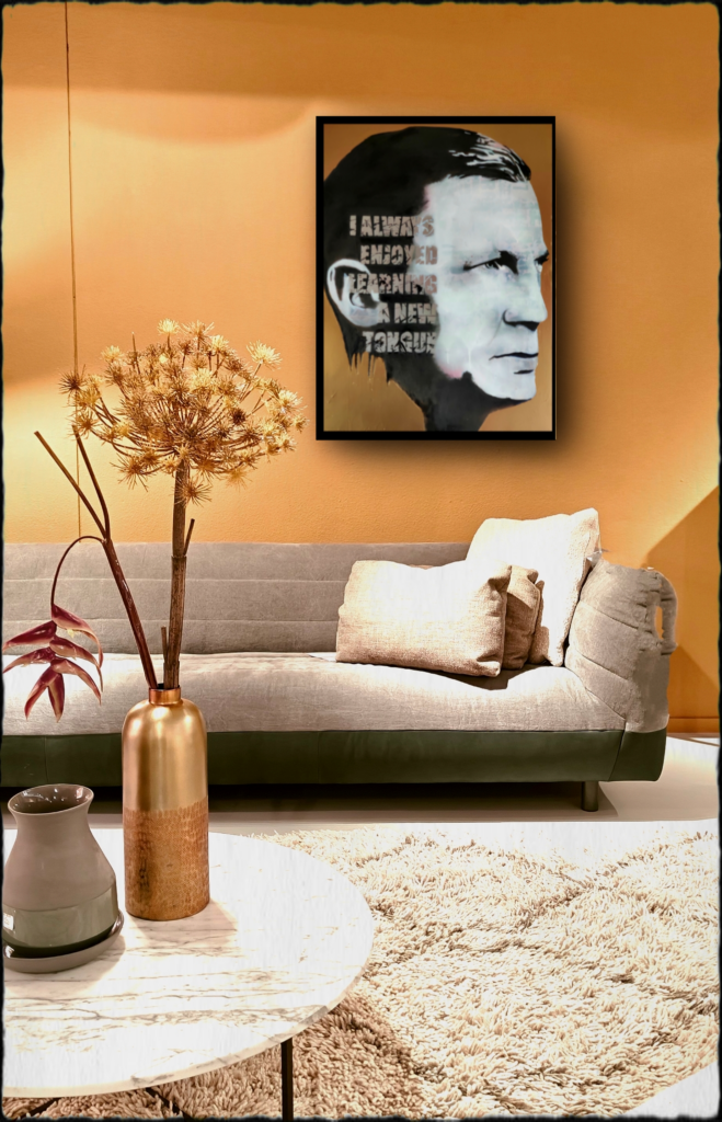 Expressief zwart-wit portret op canvas of papier in zwarte lijst, gepresenteerd boven een moderne grijze bank. De warme okergele muur, gouden vaas met droogbloemen en zachte texturen creëren een eigentijdse en sfeervolle setting waarin het kunstwerk centraal staat.