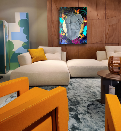 Kleurrijk hedendaags schilderij met een monochroom mannelijk torso omringd door tropische patronen, hangend boven een crèmekleurige designbank in een modern interieur met warme houtpanelen en oranje fauteuils.